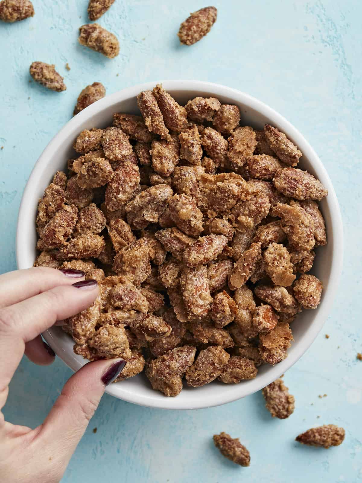 Overhead view of a bowl of candied almonds with a hand grabbing a few.