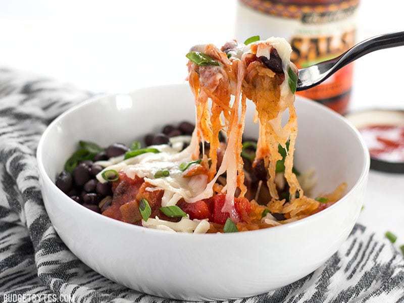 A forkful of Southwest Spaghetti Squash being lifted out of a white bowl, viewed from the side.