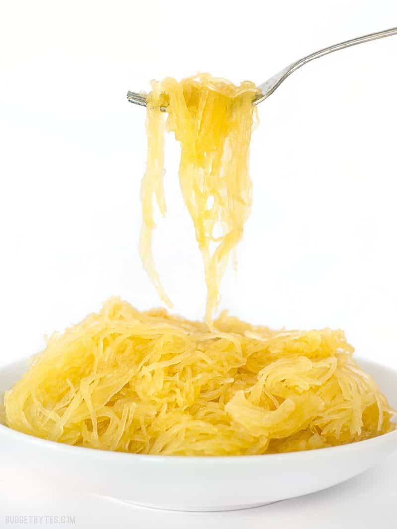 A forkful of cooked spaghetti squash being lifted out of a white bowl.