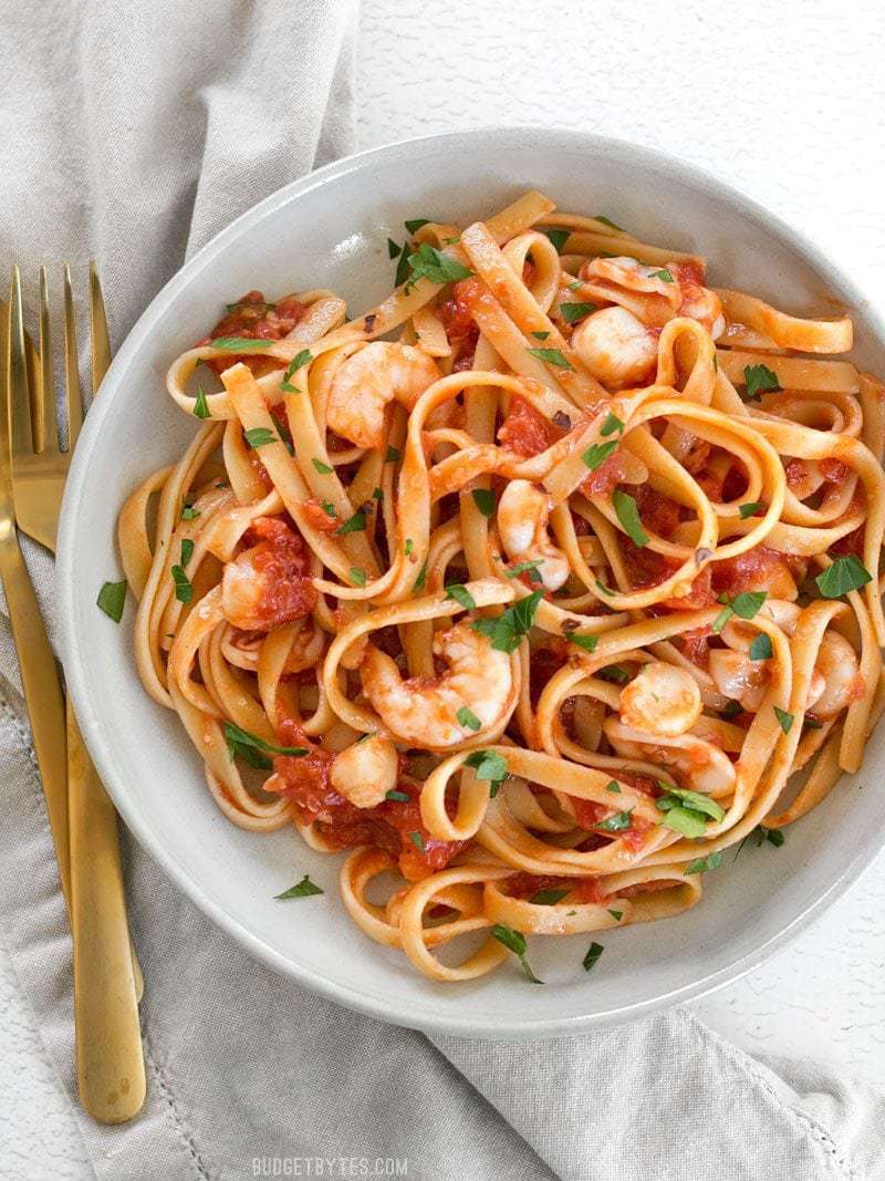 Close up overhead view of a bowl of Spicy Seafood Pasta with Tomato Butter Sauce with a gold fork and spoon on the side