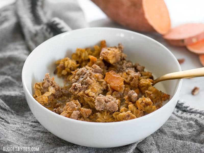 Front view of a bowl of Sweet Potato Casserole Baked Oatmeal with a gold spoon stuck into the bowl and milk poured over top.