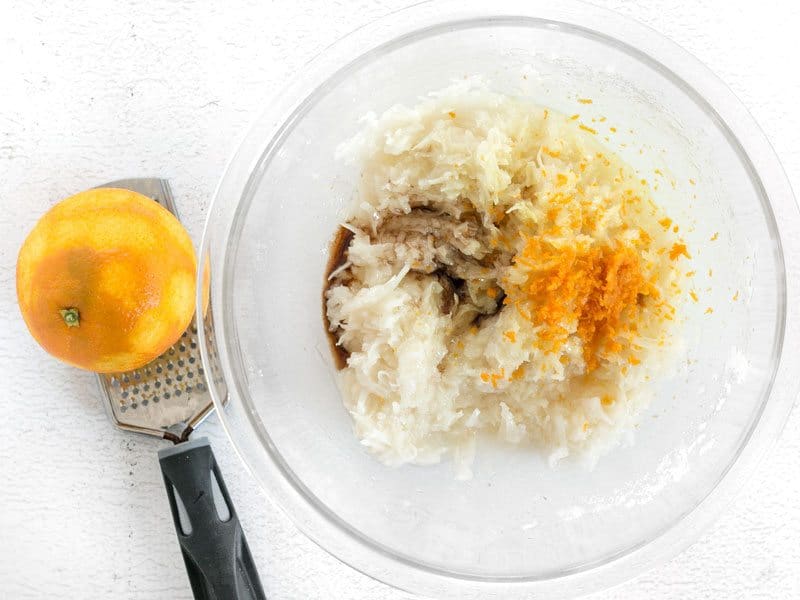 Almond extract Vanilla Extract and Orange Zest in a bowl, the orange and zester on the side