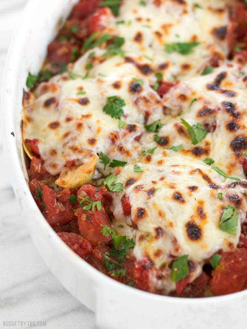 Baked Chicken with Artichokes and Tomatoes is an easy and flavorful weeknight dinner you can make with pantry staples. Budgetbytes.com Front view of Baked Chicken with Artichokes and Tomatoes in the casserole dish