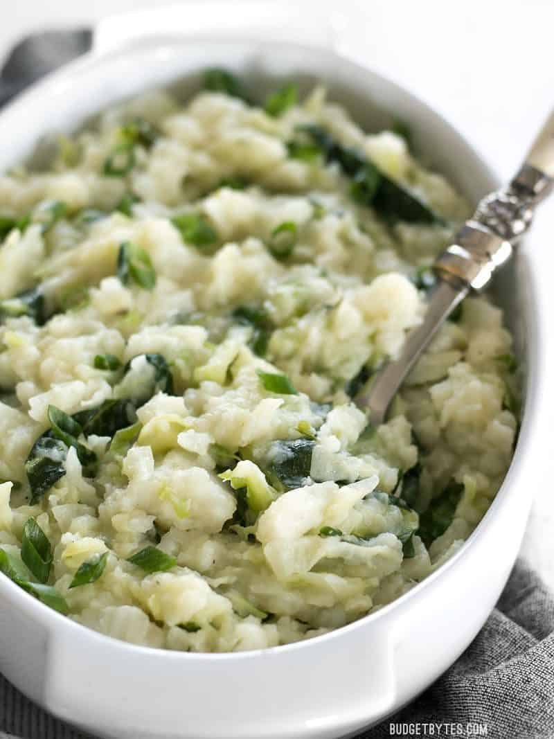 Side view of the casserole dish full of Colcannon, with a spoon stuck in the side.