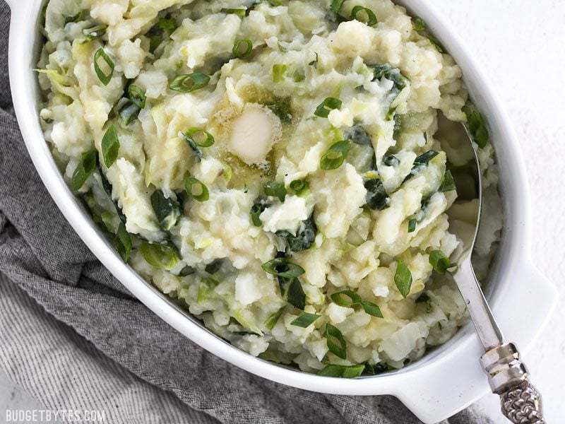 Colcannon in a white serving dish with a puddle of melted butter on top