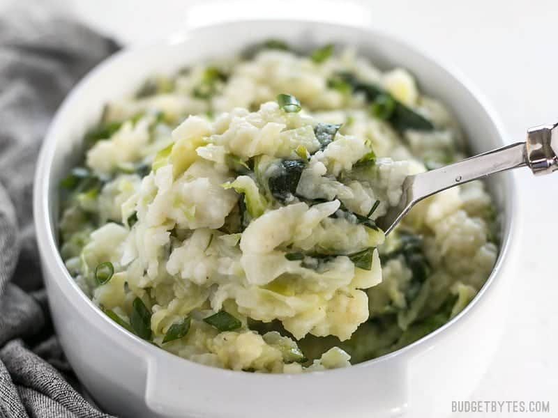 Front view of a casserole dish full of Colcannon with a big spoon lifting a heaping scoop.