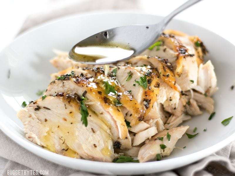 Pan juice being spooned over Herb Roasted Chicken Breast in a bowl