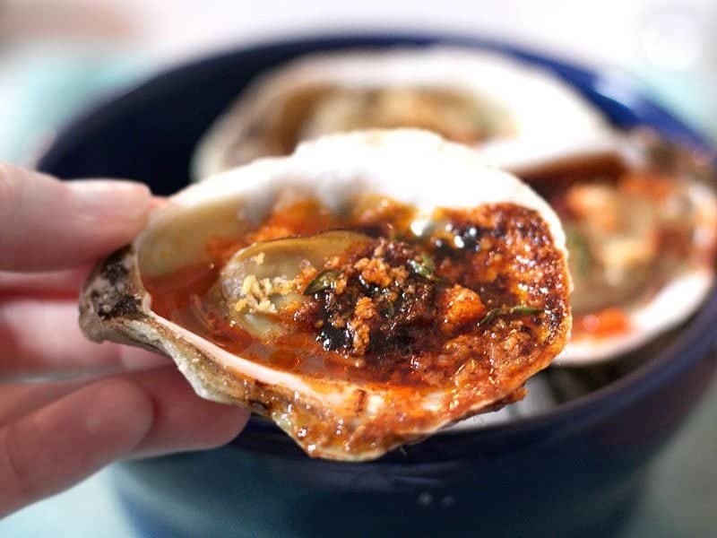 Jerk Broiled Oyster being held up by hand 