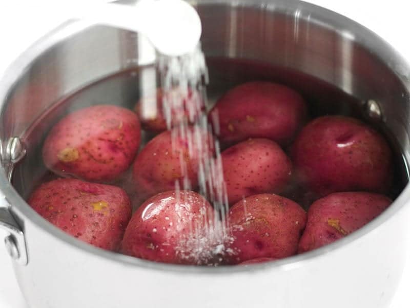 Pouring salt into pot of water and potatoes to flavor water 