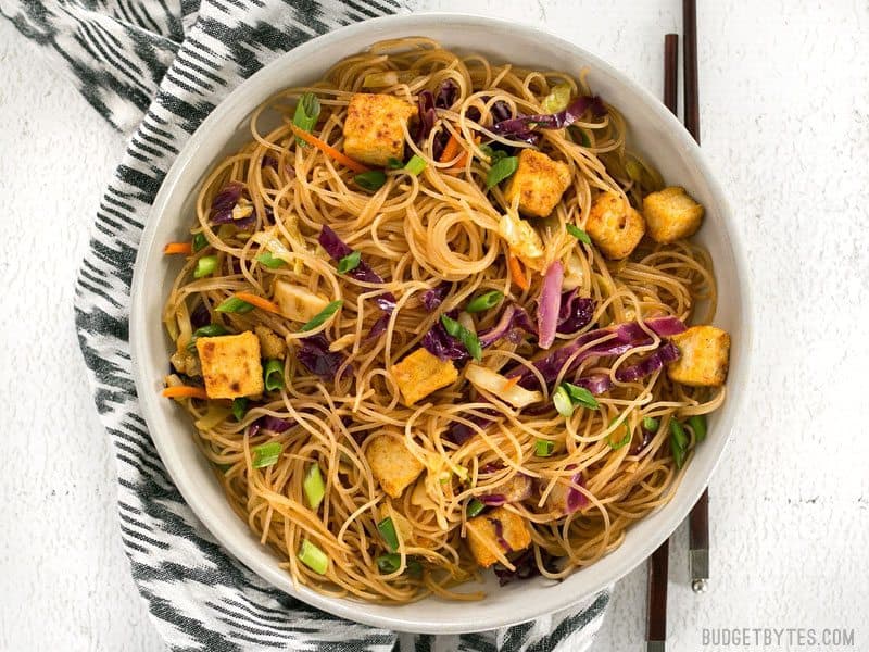 A bowl of Singapore Noodles with Crispy Tofu with chopsticks on the side