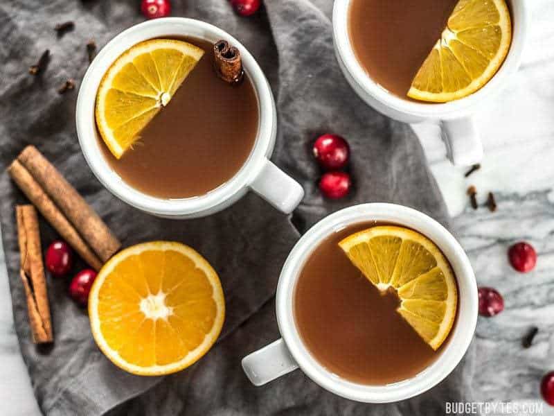 Slow Cooker Spiced Cranberry Apple Cider is an easy and festive drink for all your holiday party guests. BudgetBytes.com Three mugs of Slow Cooker Spiced Cranberry Apple Cider with garnishes, viewed from above