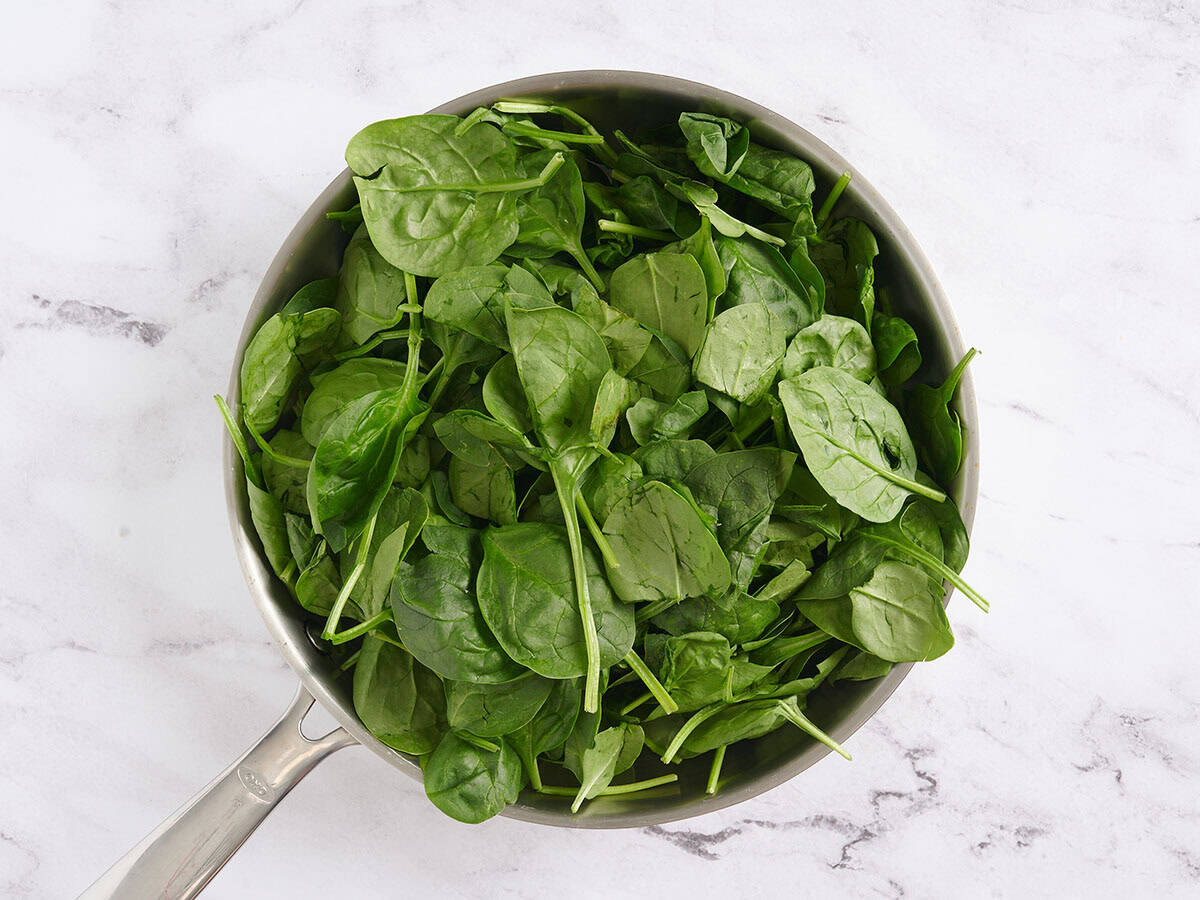 Fresh spinach added to a skillet.