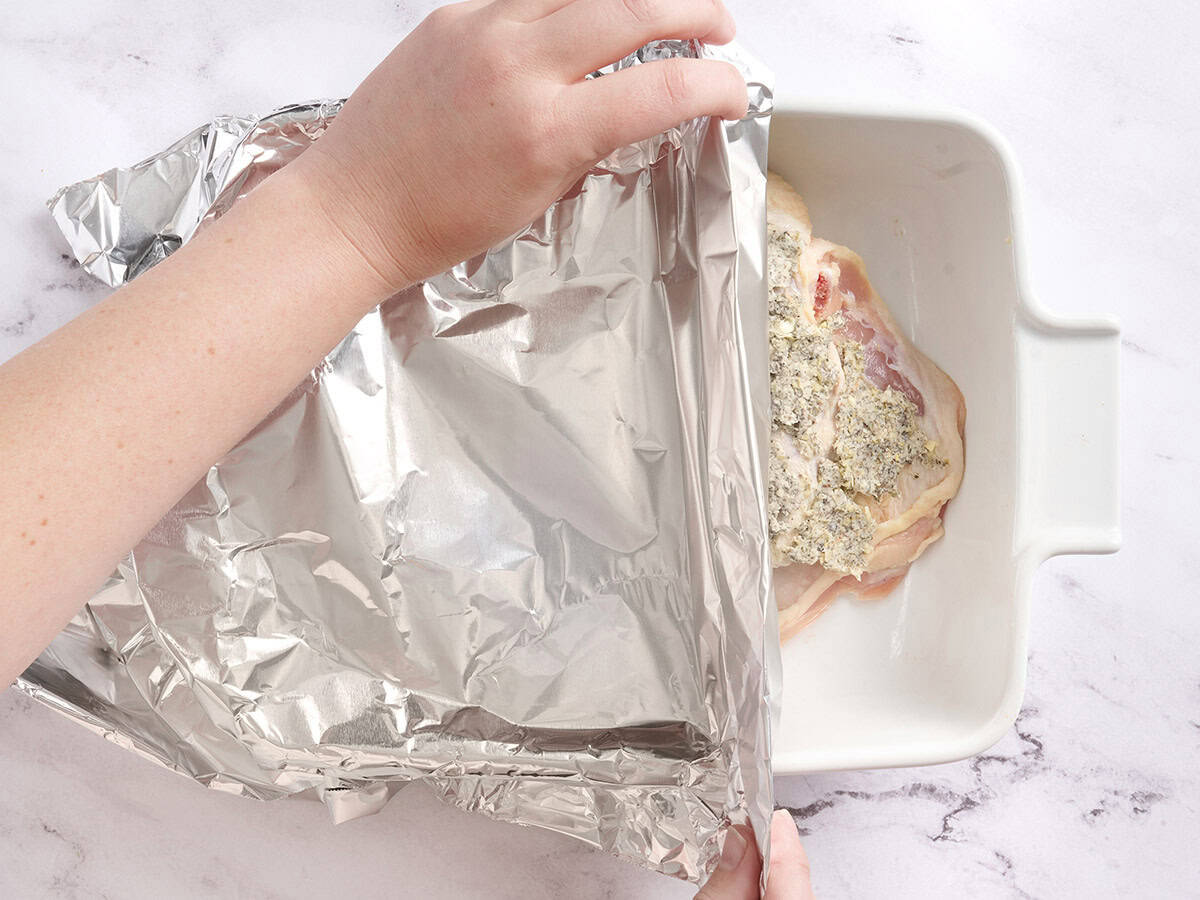 Hands covering a baking dish with foil.
