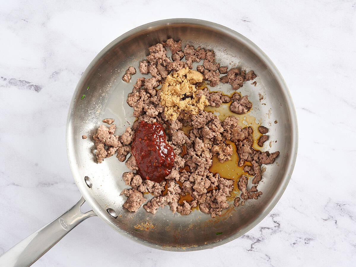 Browned ground beef in a skillet with chili sauce and brown sugar.
