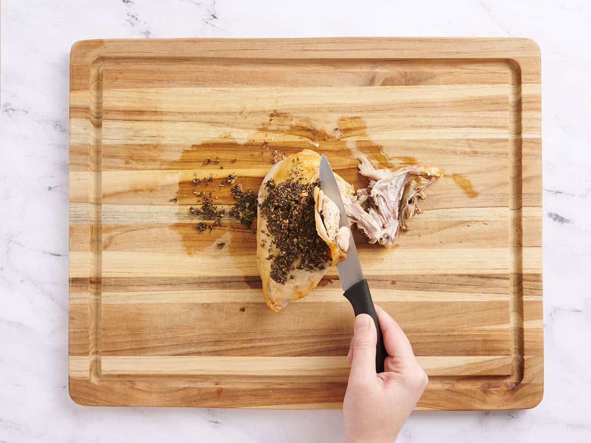 Hands deboning a bone in roasted chicken breast.