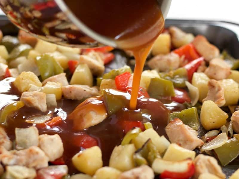 Pineapple Sweet and Sour Sauce being poured over the chicken and vegetables on the sheet pan