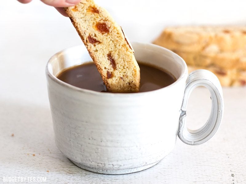 A piece of Almond Apricot Biscotti being dunked into a cup of coffee