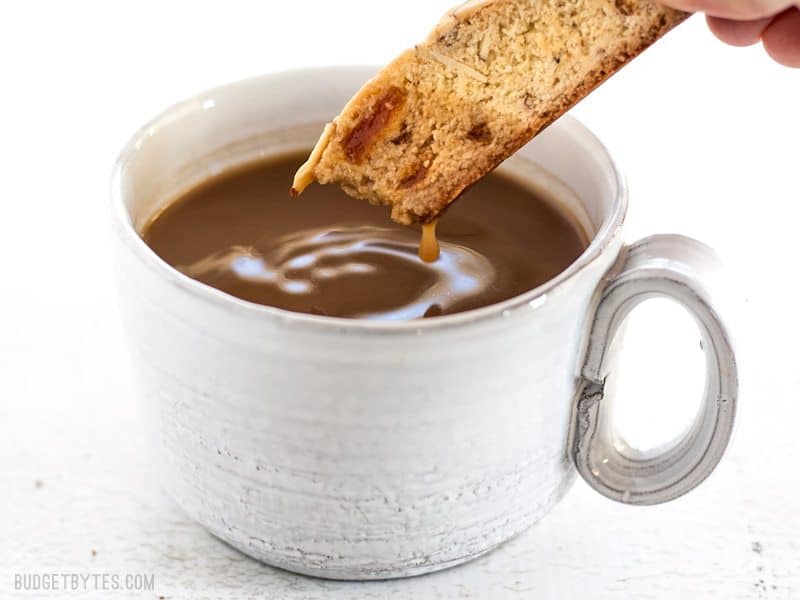 An Almond Apricot Biscotti dipped into a cup of coffee, dripping back into the cup