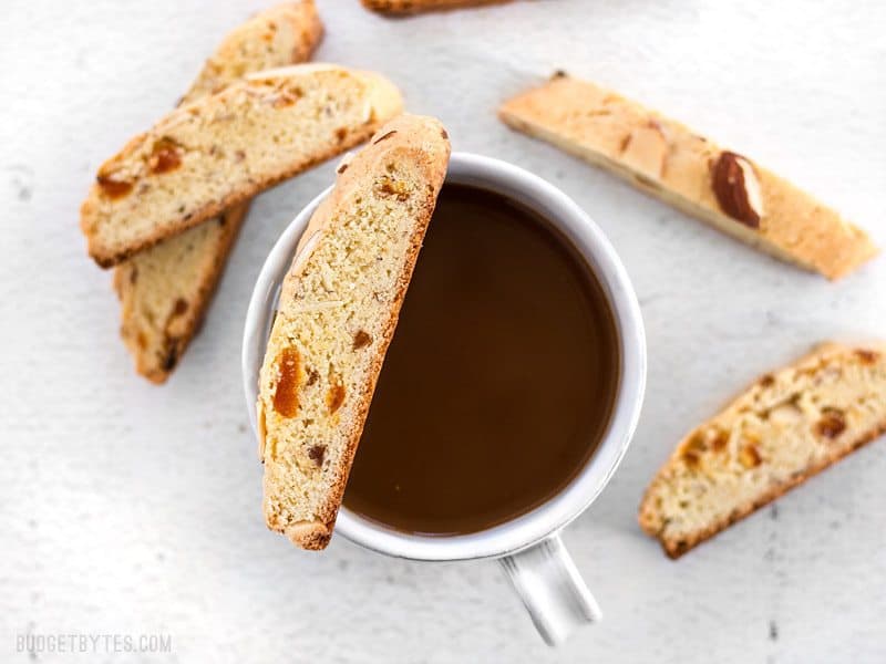 Almond Apricot Biscotti scattered around a cup of coffee, on balancing on the lip of the cup