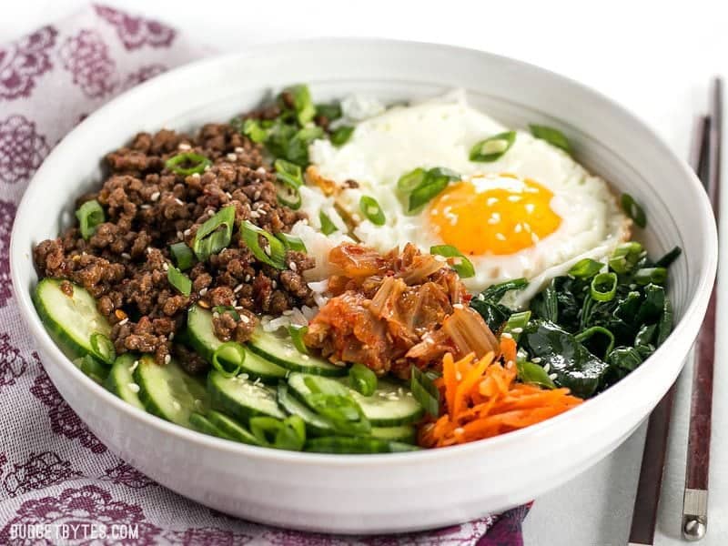Front view of a bowl of Bibimbap on a purple floral napkin.