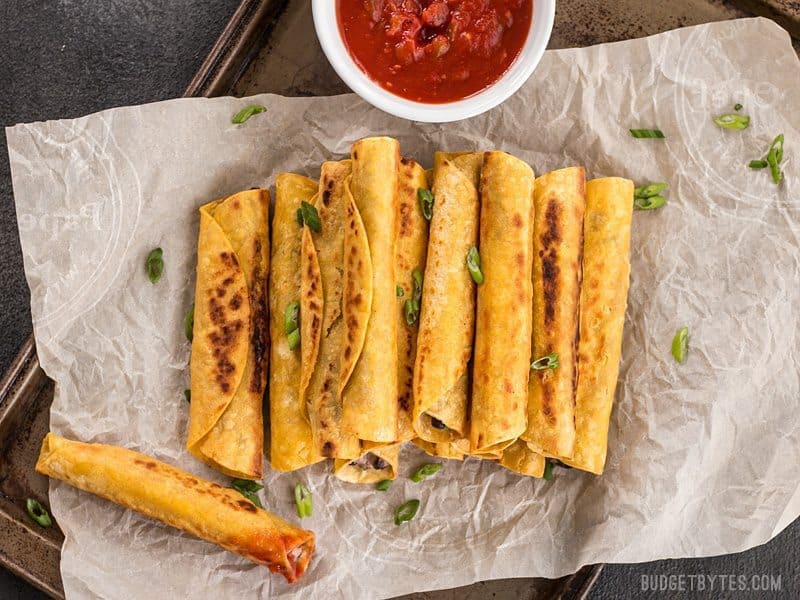 A stack of Creamy Black Bean Taquitos on a piece of parchment, one has been dipped in salsa