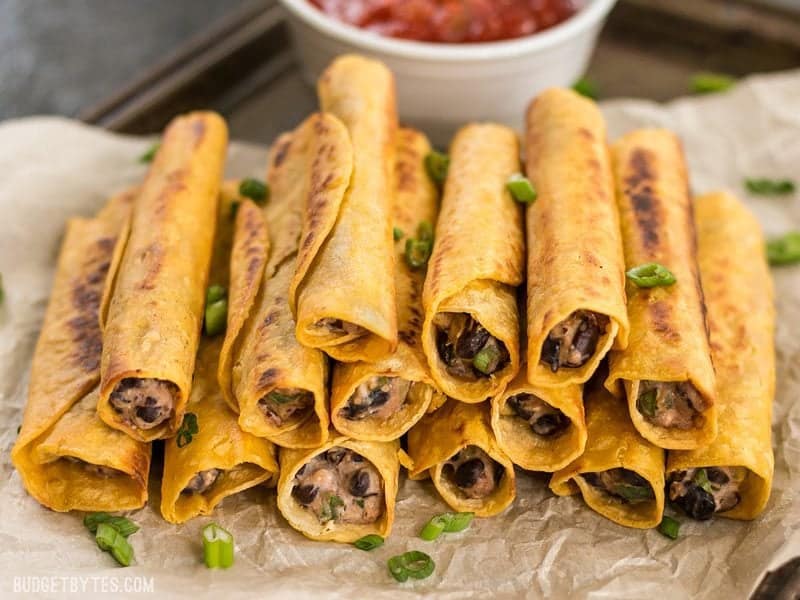 Front view of a stack of Creamy Black Bean Taquitos with a bowl of salsa in the background