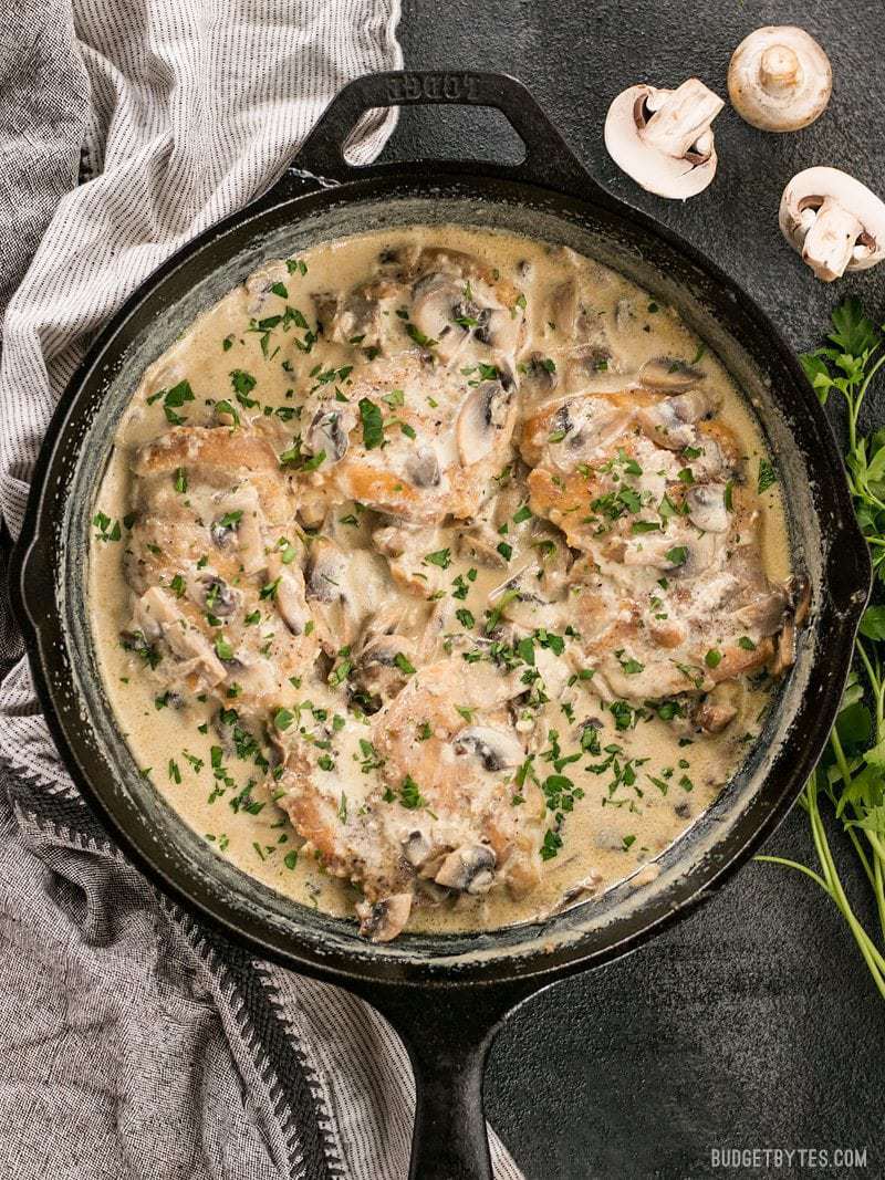 Creamy Garlic Mushroom Chicken in a cast iron skillet, garnished with parsley, whole mushrooms and parsley on the side