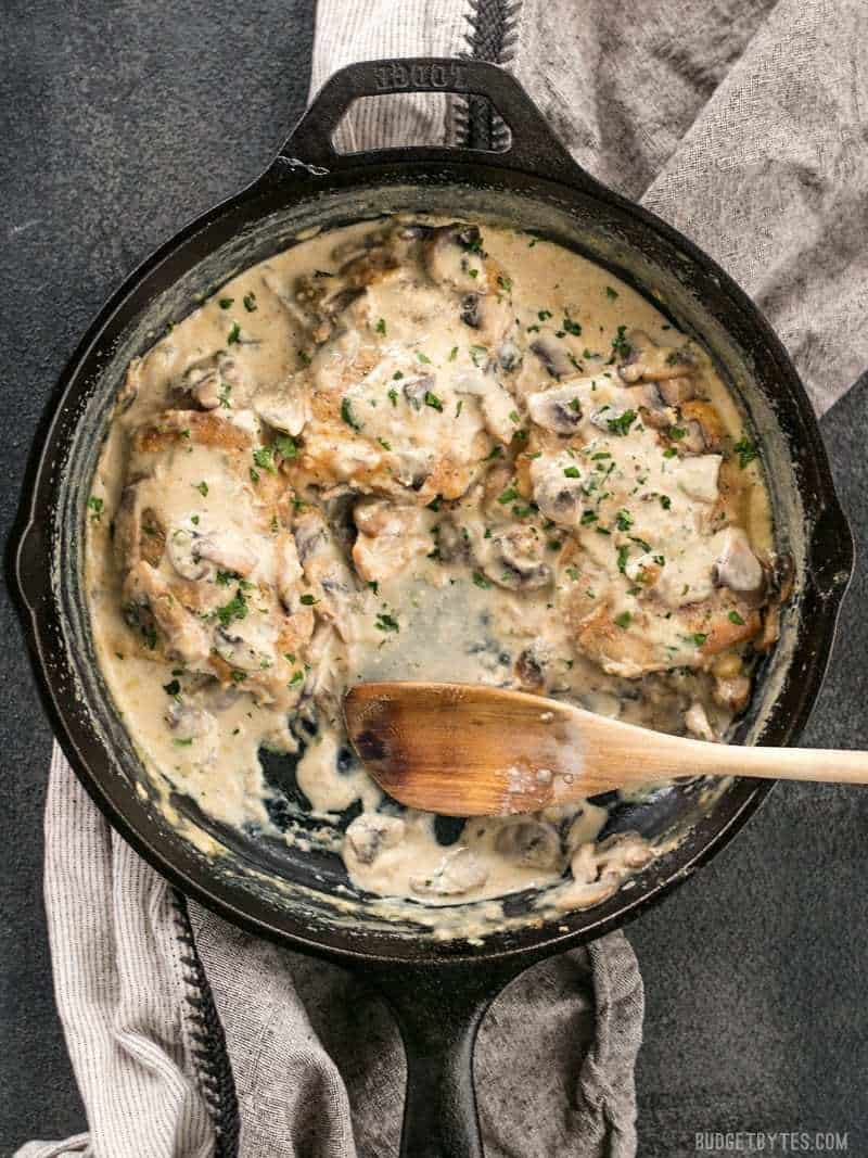 Creamy Garlic Mushroom Chicken in a cast iron skillet, with a portion missing, a wooden spoon in its place