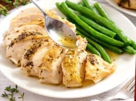 A spoon drizzling jus on a herb roasted chicken breast with green beans.