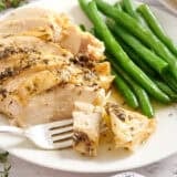 A herb roasted chicken breast with green beans on a plate with a fork.