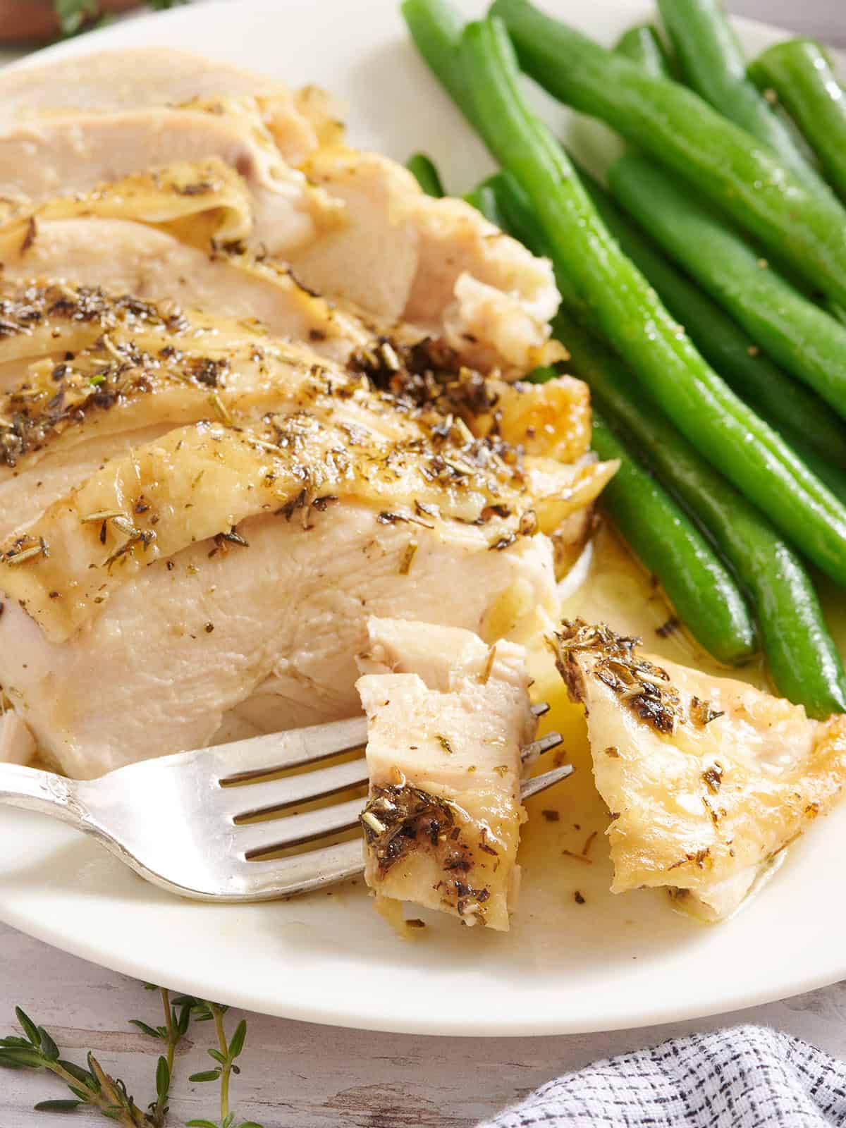 A herb roasted chicken breast with green beans on a plate with a fork.