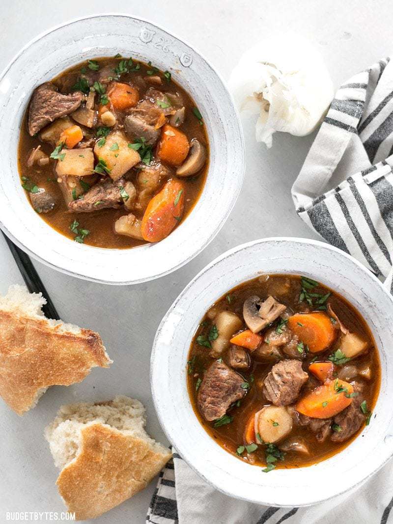 Two bowls of Instant Pot Beef Stew garnished with parsley and two torn pieces of bread on the side.