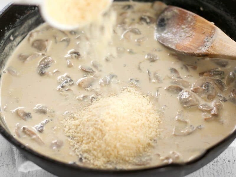 Grated Parmesan being poured into the cream sauce