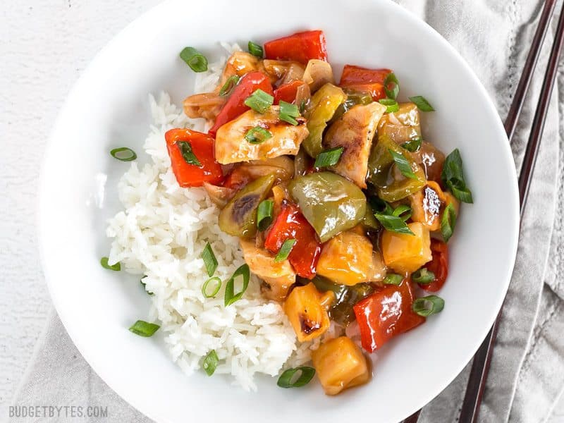 Sheet Pan Sweet and Sour Chicken in a bowl with rice, garnished with sliced green onions