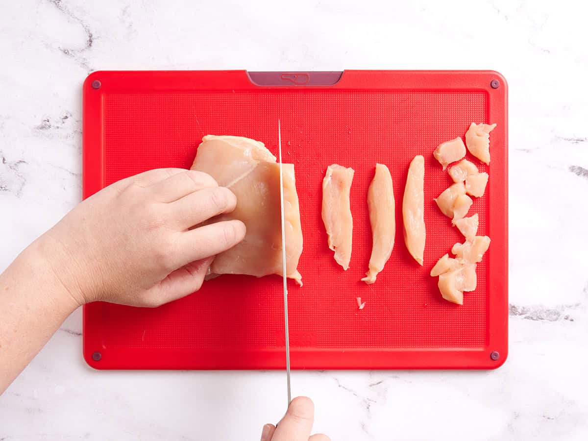 A knife slicing chicken breast into strips