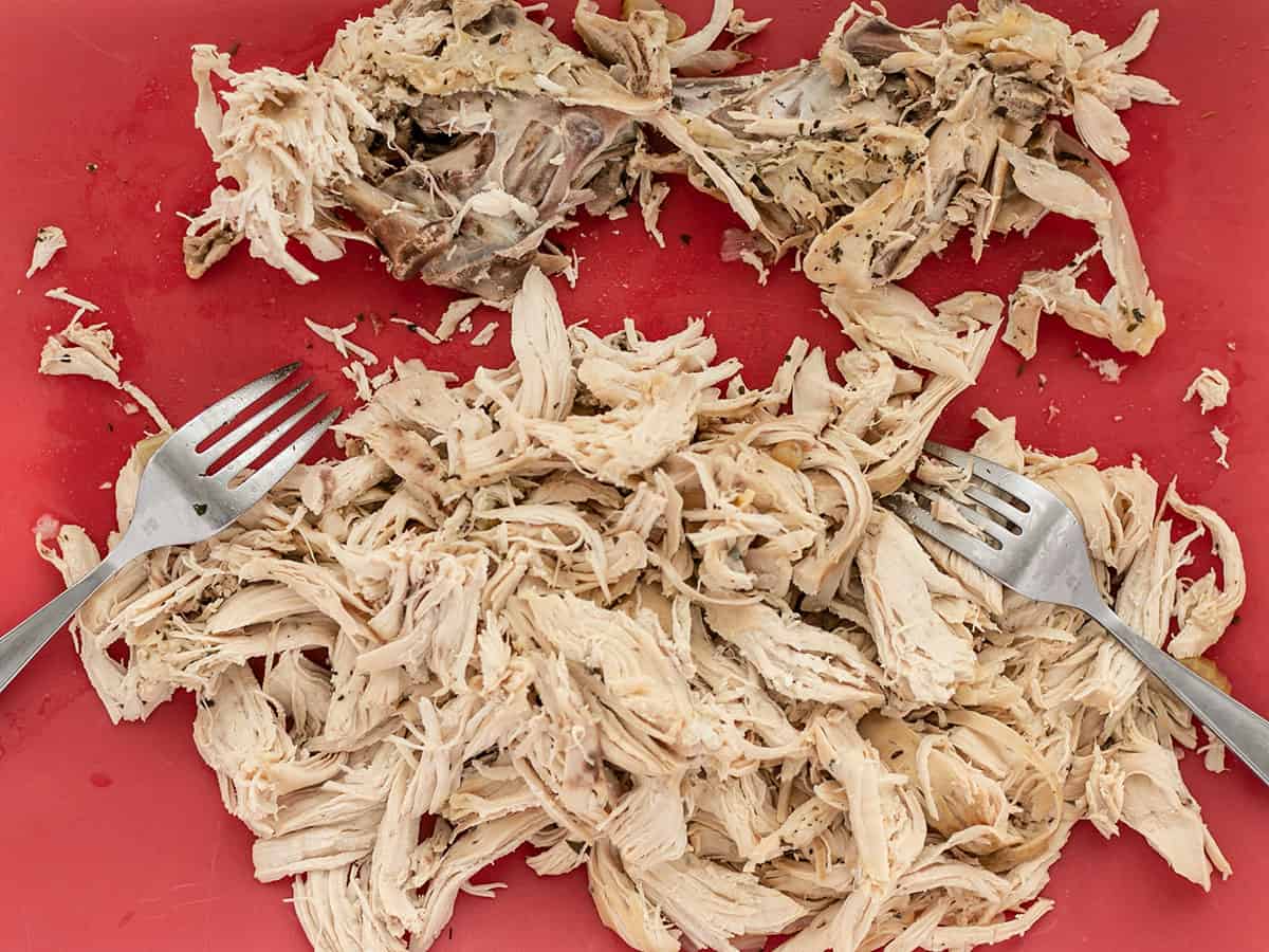 Shredded chicken with two forks on a cutting board.