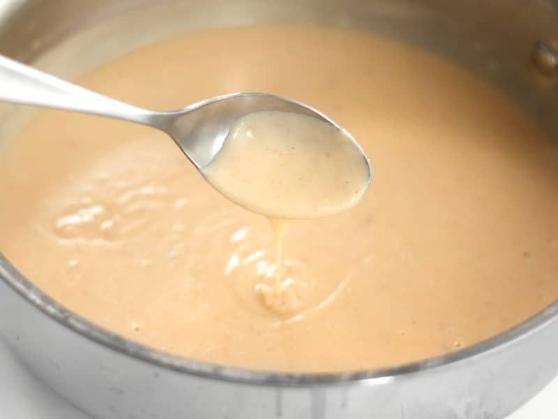 Add Milk and Spices to the creamy sauce. Thickened sauce dripping off a spoon.