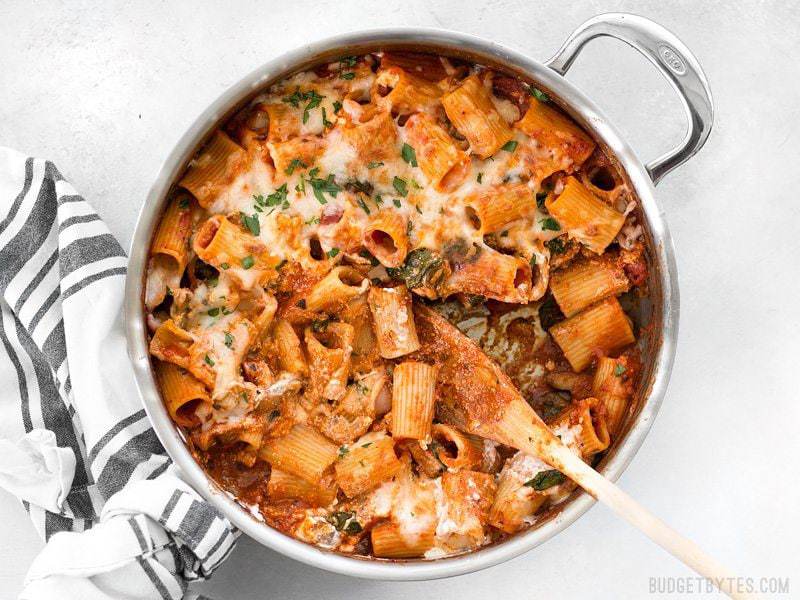 A wooden spoon scooping some Cheesy Rigatoni out of the skillet