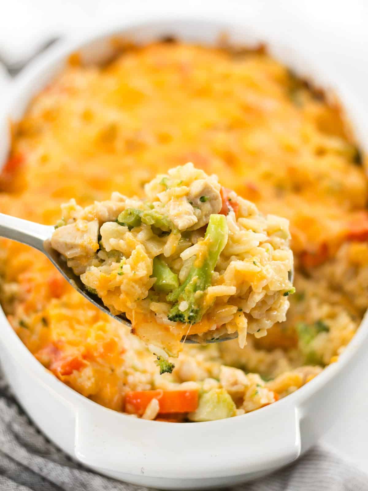 This Cheesy Chicken Vegetable and Rice Casserole is everything your comfort food dreams are made of. BudgetBytes.com Close up of a scoop of chicken and rice casserole being lifted from the baking dish.