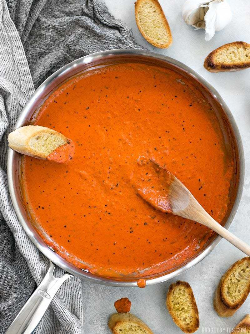 Creamy Roasted Red Pepper Sauce in a skillet with slices of bread and a wooden spoon