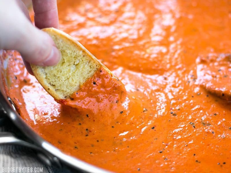 Close up of a piece of bread being dipped into Creamy Roasted Red Pepper Sauce 
