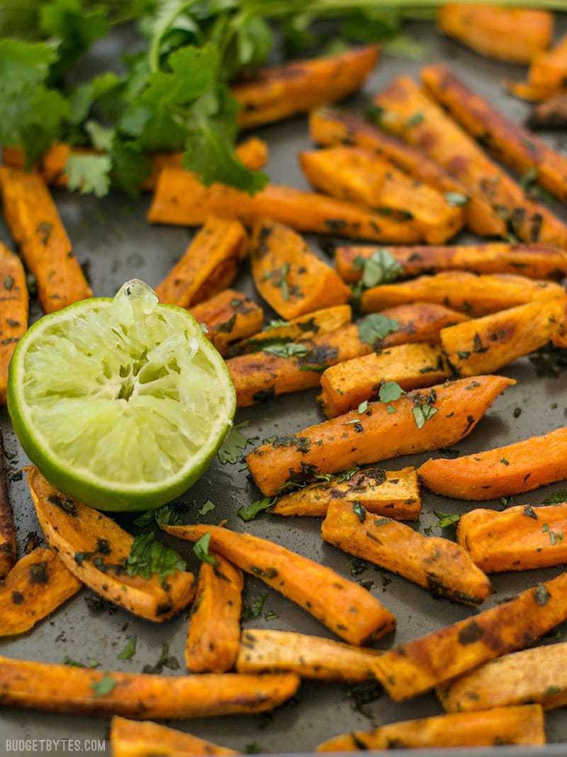 Front view of Cumin Lime Roasted Sweet Potatoes on a baking sheet with cilantro and squeezed lime