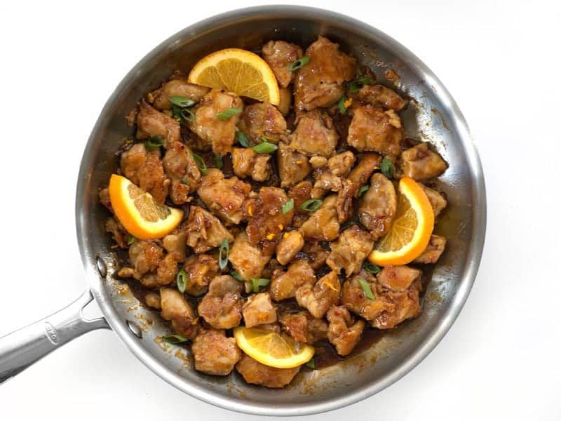 Finished Orange Chicken in the skillet garnished with orange slices and green onion