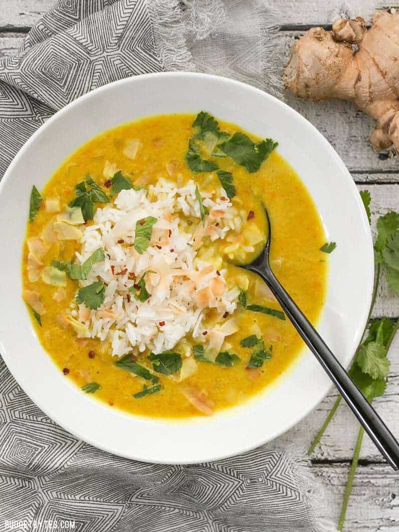 A bowl of Golden Coconut Lentil Soup with rice, coconut flakes, and cilantro on top.
