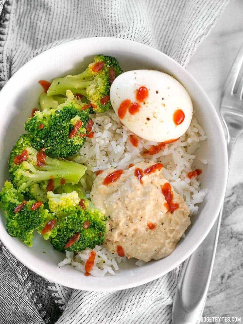 Overhead view of a Hummus Breakfast Bowl with a whole soft boiled egg and sriracha drizzled over top