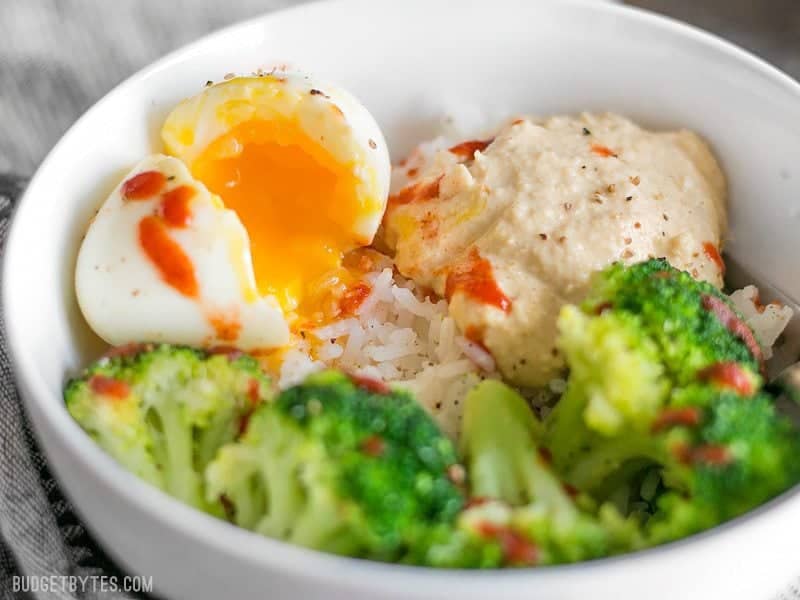 Close up side view of a Hummus Breakfast Bowl with the soft boiled egg cracked open and spilling yolk