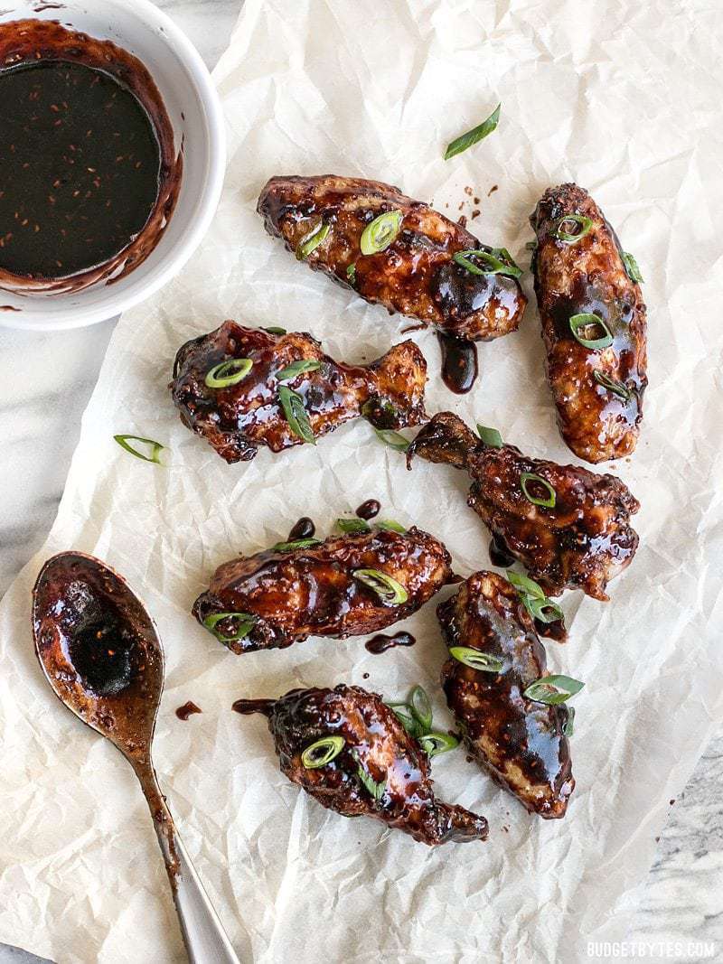 Raspberry Balsamic Baked Chicken Wings on parchment, dripping balsamic sauce, garnished with sliced green onion