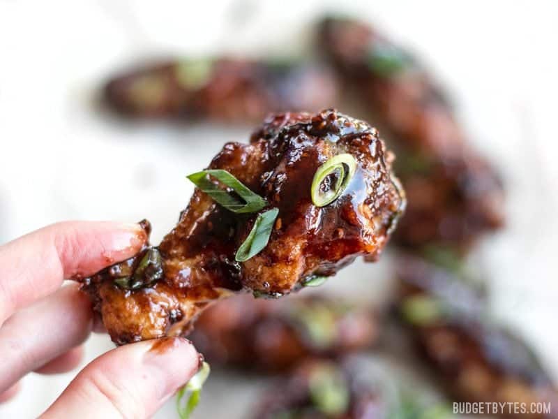 Close up of one Raspberry Balsamic Baked Chicken Wing being held in a hand, sauce getting on the fingers