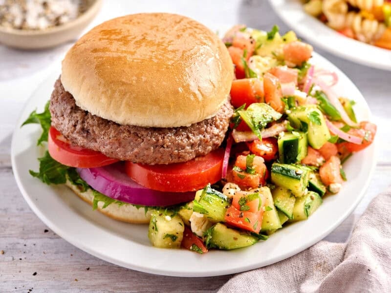 Cucumber tomato salad on a plate with a hamburger.