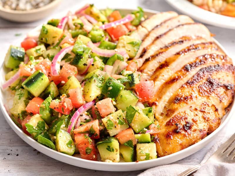 Cucumber tomato salad on a plate with sliced grilled chicken.